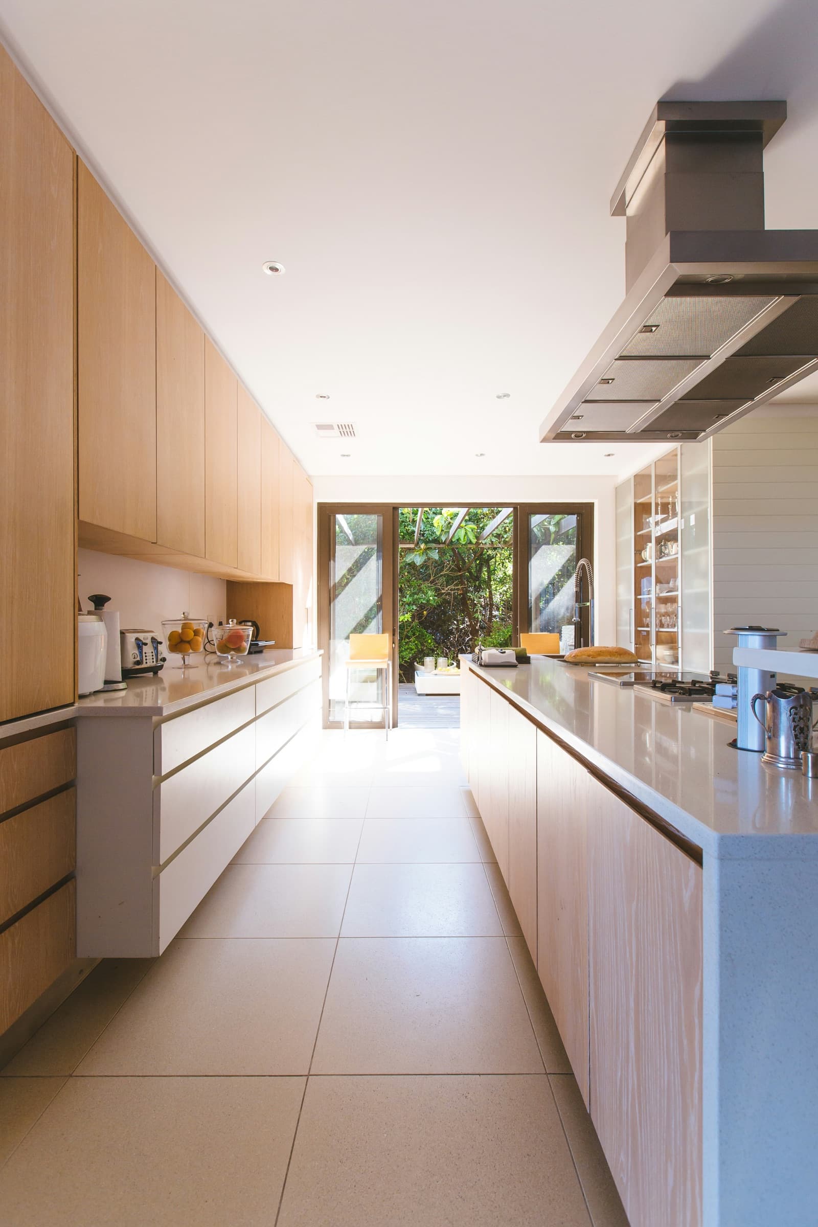 A fitted galley kitchen in pale timber opening onto a garden